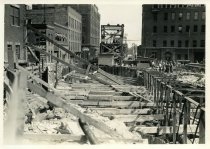 Digital scan of a sepia-toned photo taken overlooking the bracings for the excavation dug along Randolph Street during the construction of the Detroit-Windsor Tunnel, as taken from Woodbridge Street, facing south