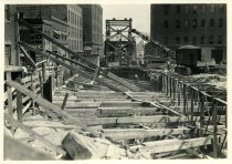 Digital scan of a sepia-toned photo taken overlooking the bracings for the excavation dug along Randolph Street during the construction of the Detroit-Windsor Tunnel, as taken from Woodbridge Street, facing south
