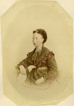 Partially hand-colorized sepia-toned portrait photograph of Ruth Campau seated, with dark hair and a full-length, long-sleeved dress