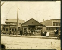 Sepia-toned photograph taken of a row of storefronts, including a grocery store, a store selling confectionaries and tobacco, and a lunch counter, possibly on Oakland Avenue between Kenilworth Street and Westminster Street