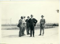 Black and white photographic print of four men gathered in discussion, smoking cigarettes at the Packard Proving Grounds