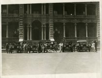 Black and white photographic print depicting circus performers posed on five Packards in front of 'Iolani Palace, Honolulu, Hawaii