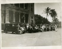 Black and white photographic print depicting circus performers posed on five Packards in front of 'Iolani Palace, Honolulu, Hawaii