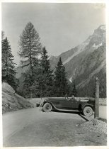Black and white photographic print of a left side profile view of a Packard 8 convertible being driven around a bend in the Swiss Alps