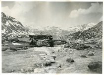 Black and white photographic print showing a right side view of a Packard 8 convertible parked along a stream in the Swiss Alps