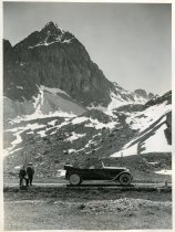 Black and white photographic print showing a right side profile view of a Packard 8 convertible parked on a road in the Swiss Alps, with mountains visible in the background