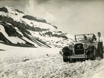 Black and white photographic print featuring a front end view of a Packard 8 convertible on a snow covered road in the Swiss Alps