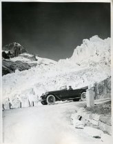 Black and white photographic print showing a left side view of a Packard 8 convertible on a mountain road in the Swiss Alps