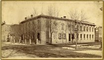 Cabinet card bearing a sepia-toned panoramic photograph taken of the exterior of Herman Kiefer's office at 52 Gratiot Avenue from the intersection of Gratiot and Farrar Street