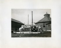 Black and white photographic print taken outside depicting a Packard automobile from the front surrounded by 12 white horses on their hind legs