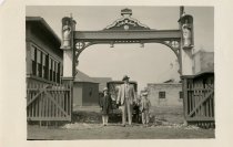 Black and white photographic print taken outside depicting a Packard automobile from the front parked under an archway