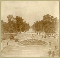 Mounted sepia-toned photo of a view along Belle Isle's Central Avenue as taken from an elevated positioned overlooking an island with a floral arrangement in the center of the road