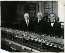 Photograph of three men and a model of a moving sidewalk