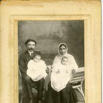 Matted black and white photo of seated couple holding babies in their laps