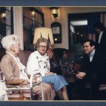 Color photo of Spencer Abraham w two elderly women with flags behind