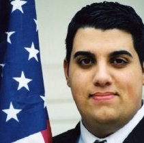 Color photo of Nicola Hawatmeh headshot standing next to American flag