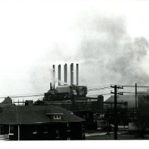 Black & white photo of factory in background with house in foreground.
