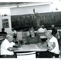 Black & white photo of older men sitting at a table playing dominoes