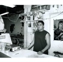 Black and white photo of young man standing behind a shop counter