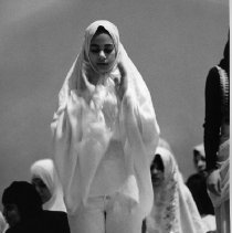 Black and white image of a girl in white hijab and jeans standing in prayer