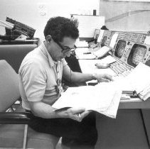 Black and white photo of El-Baz sitting at control desk reading paper chart