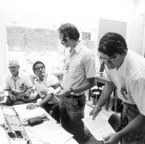 Black and white portrait of four men reading charts and graphs