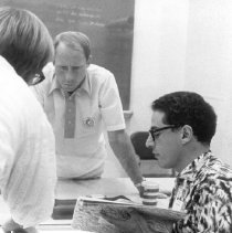 Black and white photo of El-Baz seated with books and two men standing