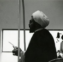 Photo of profile of imam mid-speech hoding a paper in his hands