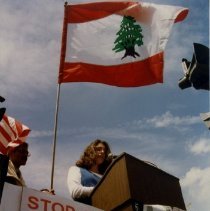 Color photograph of teen giving speech at podium under Lebases flag
