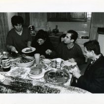 Black & white photo of adults sitting at kitchen table with food