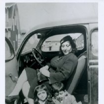 Black & white photo of woman in drivers seat of car with two kids sitting i