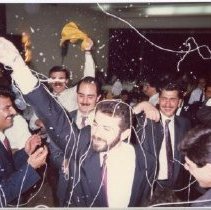 Color photograph of men in suits w silly string in the air