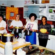 Color photo of four women in kitchen holding pots of food