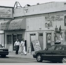 Black and white photo of men walking in front of storefronts