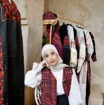 Photo of Bayan Fares posing infront of her handmade Palestinian Tatreez