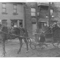 Bernie Douglas in front of the City Hotel (later the YMCA), Guelph, Ontario. Parcel Delivery onside of sleigh, ca. 1900.