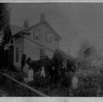 Clapboard house with 2 men, woman and 2 little girls standing in garden identified as John Prain, his house and garden in Harriston, ON, ca. 1900.