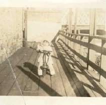 Joy Lorraine Davies, daughter of Fred Davies, on last kiddie car made at the Canadian Kiddie Kar Co. Ltd., Elora, ON. On the Boardwalk, Mill St., Elora; Metcalfe St. Bridge in background, ca. 1939-1940.