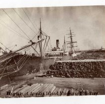 Photograph of ships and lumber at the docks.