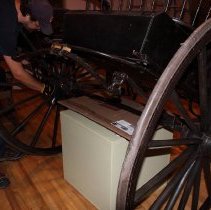 Man removing a wheel from a two-wheeled carriage