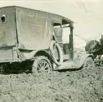 Automobile being pulled out of the mud by a 2 horse team.