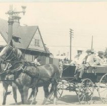 Two horses pulling a small open carriage with four men aboard