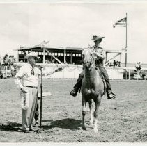 man at a microphone welcoming a woman on horseback