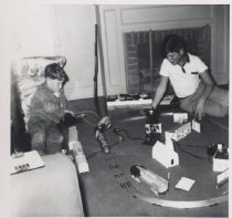 Two Boys Play with Toy Trains on Floor in Front of Fireplace