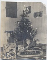 Two Children Play with Train Under Tree Lit by Candles