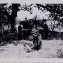 Soldier Aims Rifle with 155mm Howitzer behind him at a WWII Training Camp