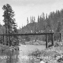 Crew preparing railroad bridge for train wreck scene. Spectators visible.
