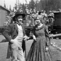 Actors posing on set with cast on train in background.