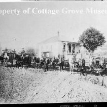 Group of horse drawn vehicles with drivers posed in front of house