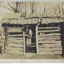 Three women standing beside a small log building (ca. 1910-1920)